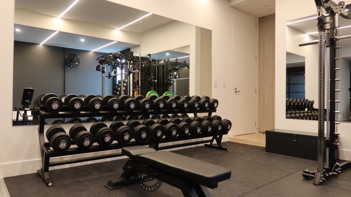 Finished garage gym with mirror walls, LED strip lighting, rubber flooring and a full dumbbell rack