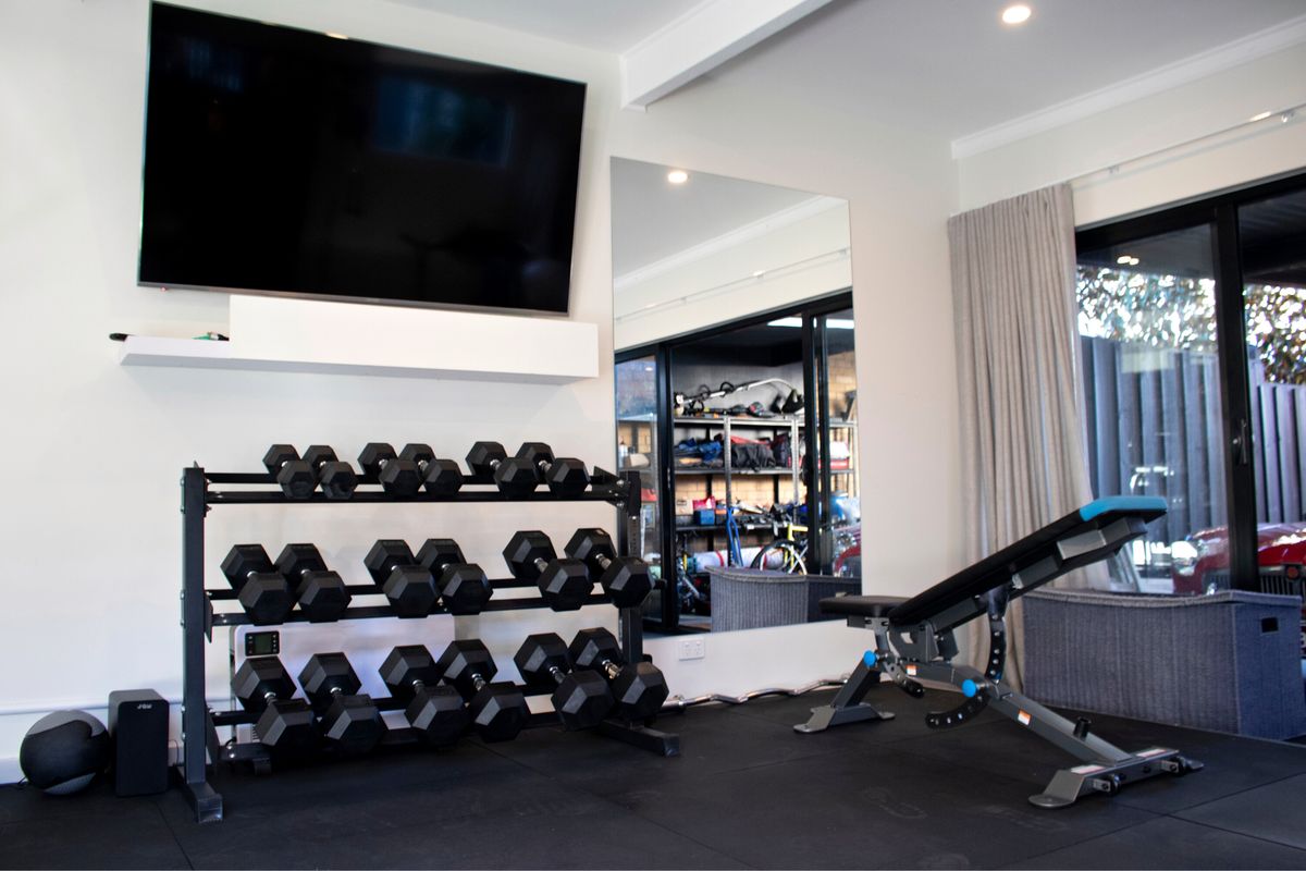 Home gym with wall-mounted TV, mirror, dumbbell rack and adjustable bench