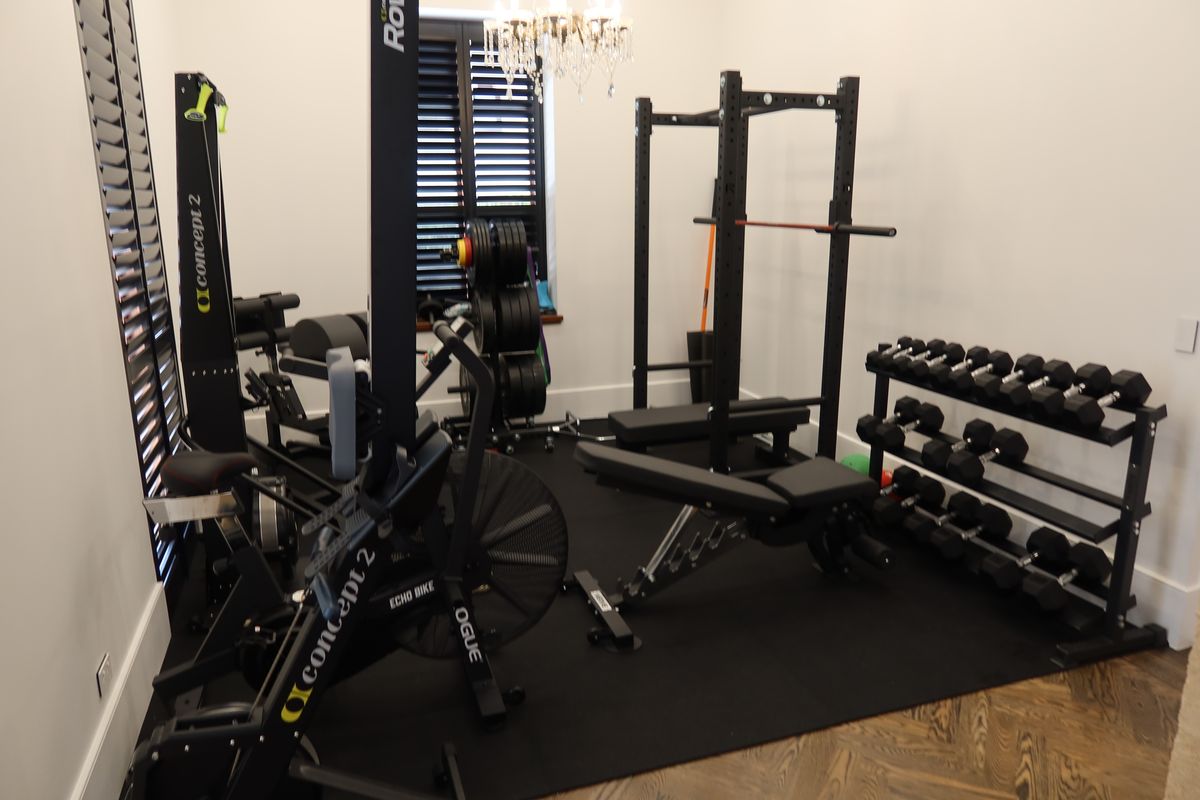 Spare room converted into a home gym with rack, bench, rower and bike